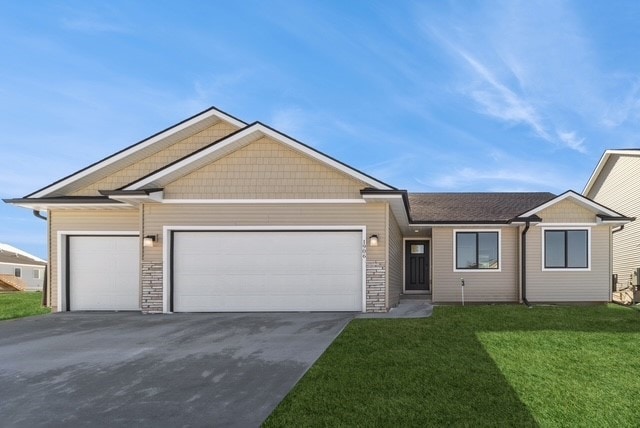 view of front of home with driveway, stone siding, an attached garage, and a front yard