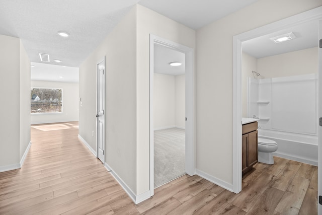 hallway featuring light wood finished floors, visible vents, and baseboards