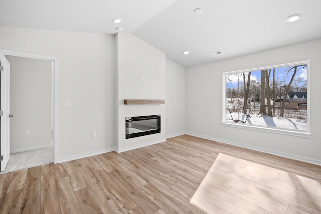 unfurnished living room with light wood-type flooring, a glass covered fireplace, vaulted ceiling, and baseboards