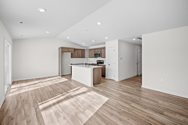 kitchen with light wood-style flooring, stainless steel appliances, open floor plan, light countertops, and an island with sink