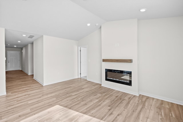 unfurnished living room featuring lofted ceiling, visible vents, light wood-style flooring, a glass covered fireplace, and baseboards