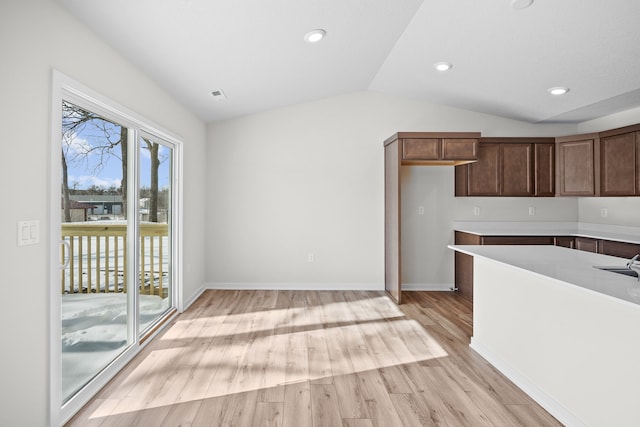 kitchen with lofted ceiling, light countertops, light wood-style flooring, and baseboards