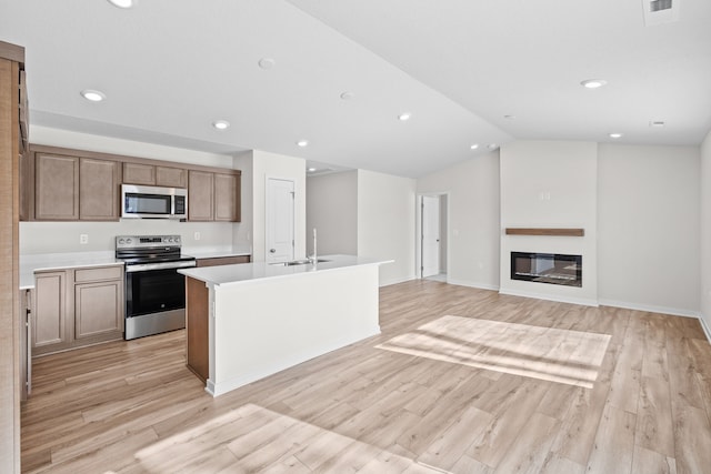 kitchen with a glass covered fireplace, appliances with stainless steel finishes, open floor plan, a kitchen island with sink, and light countertops