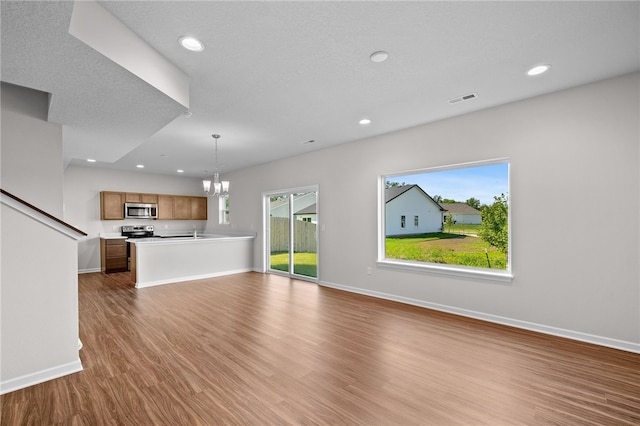 unfurnished living room featuring an inviting chandelier, sink, a textured ceiling, and light wood-type flooring