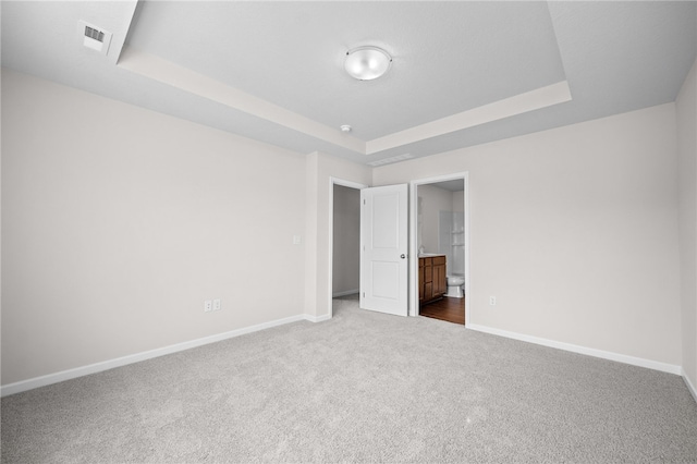 unfurnished bedroom with ensuite bathroom, a raised ceiling, and carpet