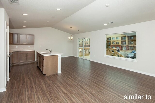 kitchen with sink, dark hardwood / wood-style floors, pendant lighting, vaulted ceiling, and a kitchen island with sink