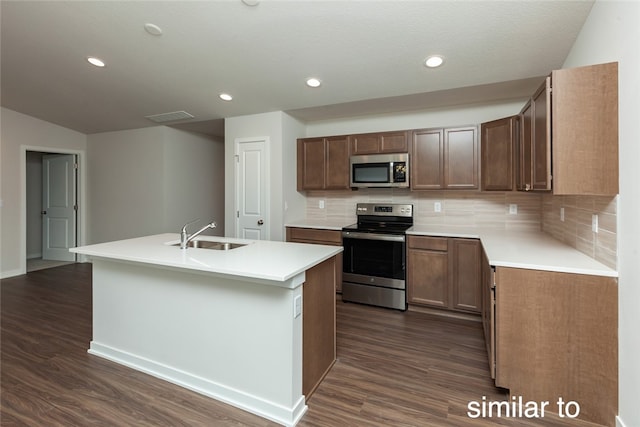 kitchen featuring dark wood-type flooring, stainless steel appliances, a center island with sink, and sink