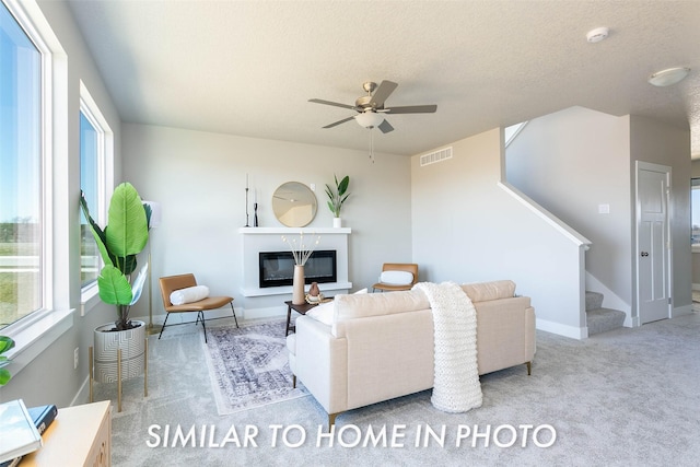 carpeted living room featuring ceiling fan and a textured ceiling