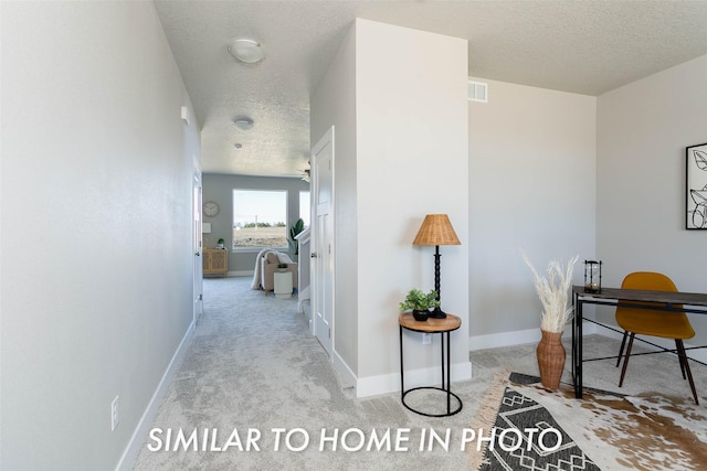 hallway with light carpet and a textured ceiling