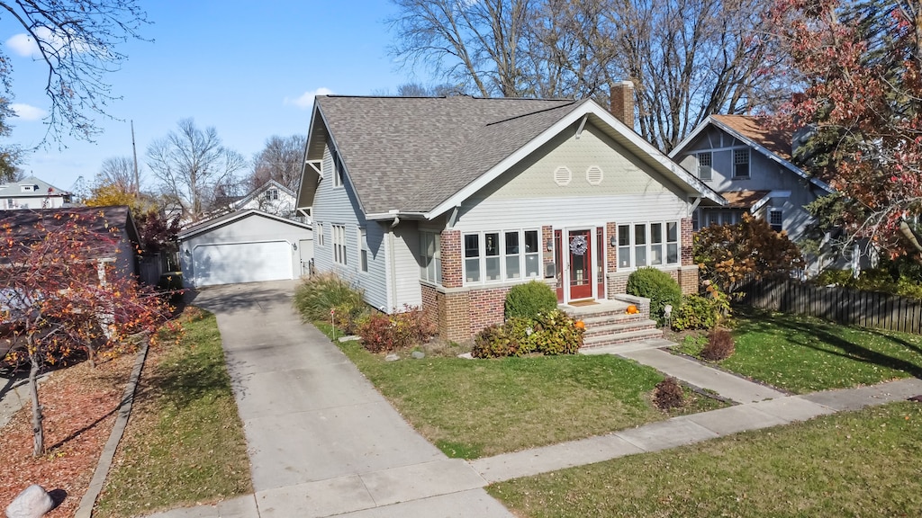 bungalow featuring a front lawn, a garage, and an outbuilding