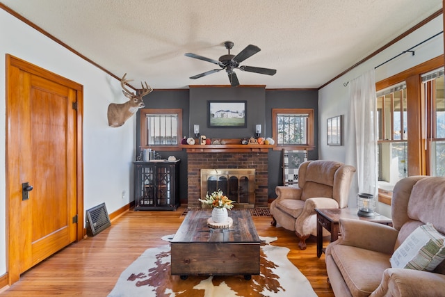 living room featuring ornamental molding, ceiling fan, a textured ceiling, a fireplace, and light wood-type flooring