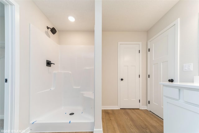 full bath with a textured ceiling, wood finished floors, vanity, baseboards, and walk in shower