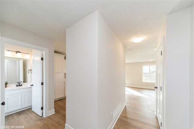 hall featuring light wood-type flooring, a sink, visible vents, and baseboards