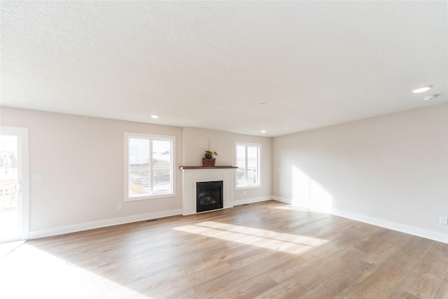 unfurnished living room with a textured ceiling, light wood finished floors, a fireplace, and baseboards