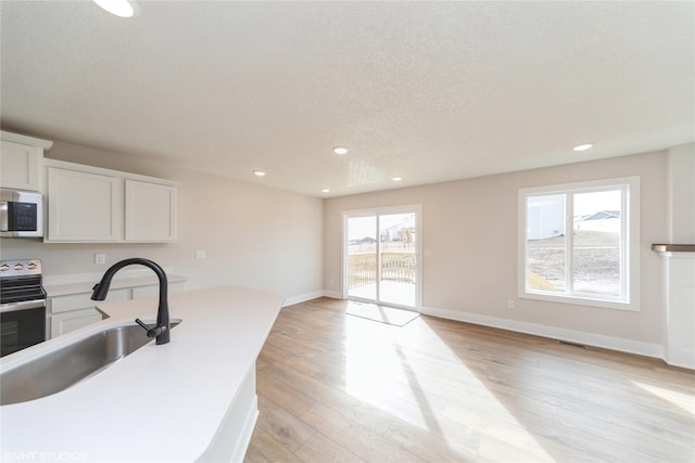 kitchen with baseboards, electric range oven, white microwave, light wood-style flooring, and a sink