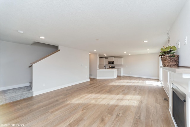 unfurnished living room featuring recessed lighting, a fireplace, baseboards, stairway, and light wood-type flooring