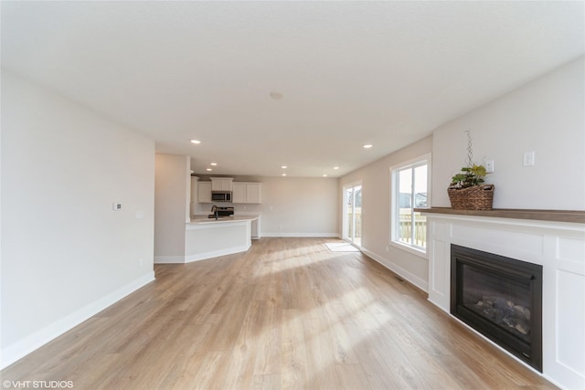 unfurnished living room featuring a glass covered fireplace, light wood-style flooring, baseboards, and recessed lighting