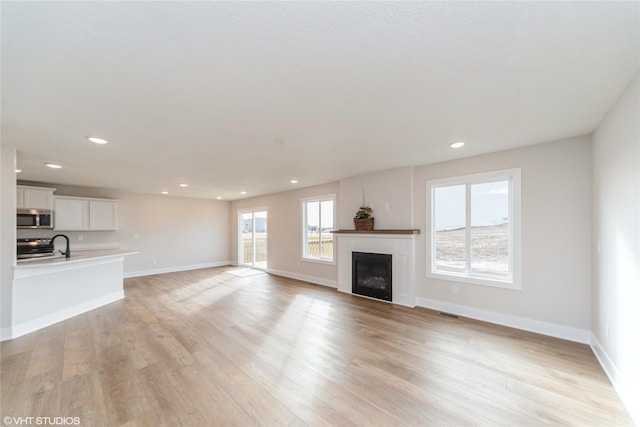 unfurnished living room with light wood finished floors, recessed lighting, a glass covered fireplace, and baseboards