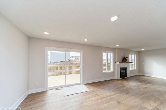 unfurnished living room with light wood-style floors, baseboards, visible vents, and a glass covered fireplace