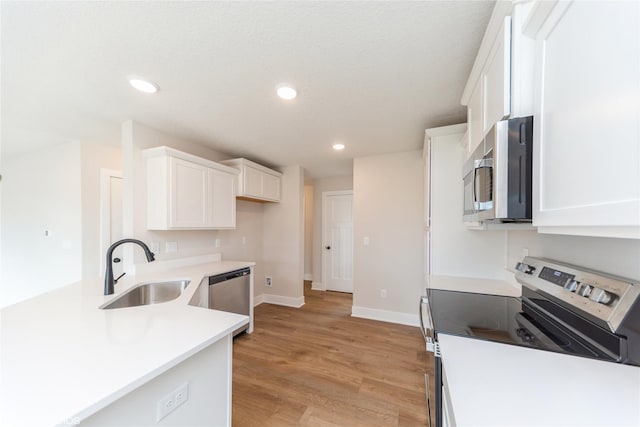 kitchen featuring white cabinets, appliances with stainless steel finishes, light wood-type flooring, a sink, and recessed lighting