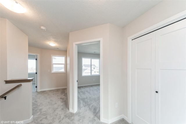 corridor featuring light carpet, baseboards, a textured ceiling, and an upstairs landing