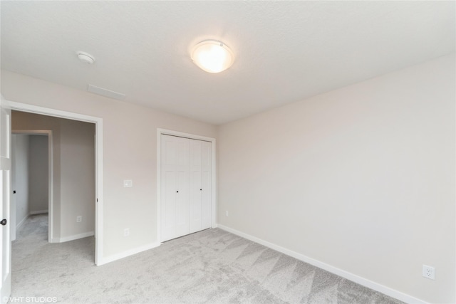 unfurnished bedroom with a closet, light carpet, and baseboards