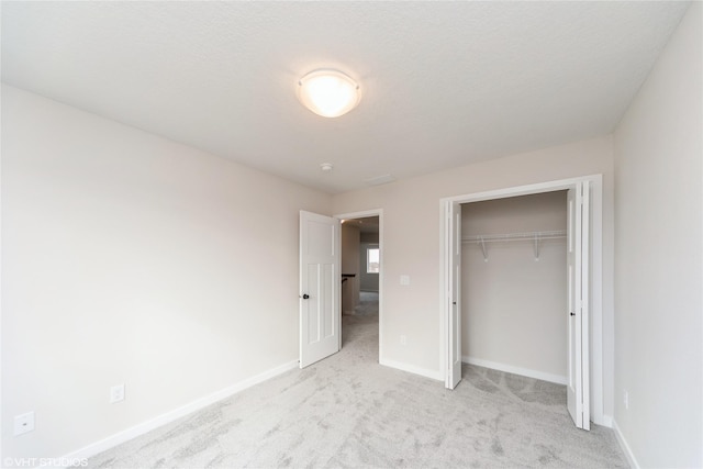 unfurnished bedroom with a closet, light colored carpet, and baseboards