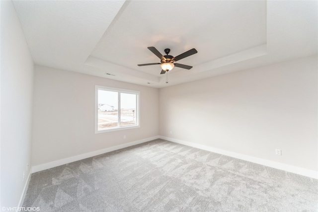 carpeted empty room with a raised ceiling, visible vents, ceiling fan, and baseboards