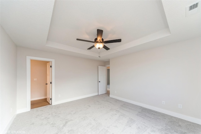 empty room with a tray ceiling, visible vents, and baseboards