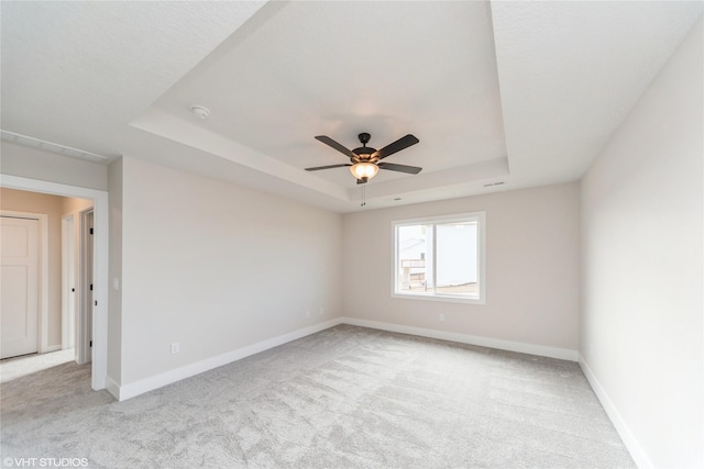 carpeted spare room featuring a ceiling fan, a tray ceiling, and baseboards