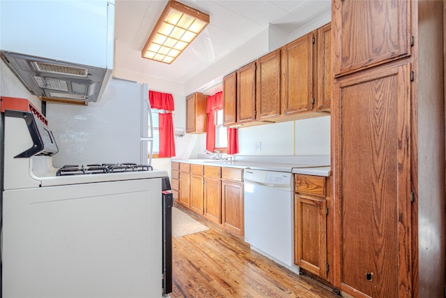 kitchen with light wood-type flooring, exhaust hood, sink, and white appliances