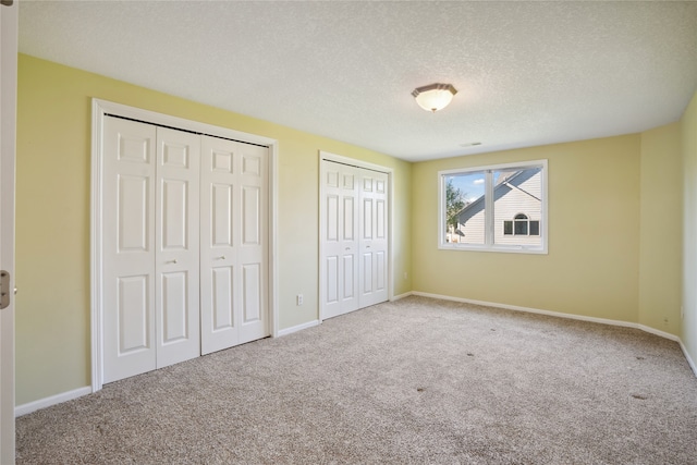 unfurnished bedroom featuring two closets, a textured ceiling, and carpet floors