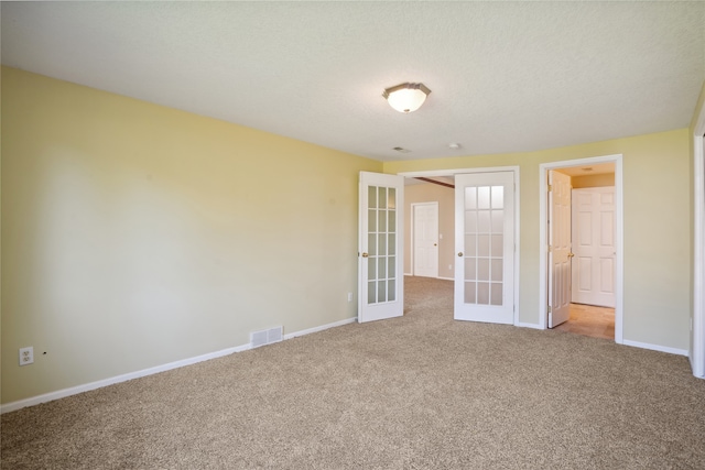 carpeted empty room with french doors and a textured ceiling