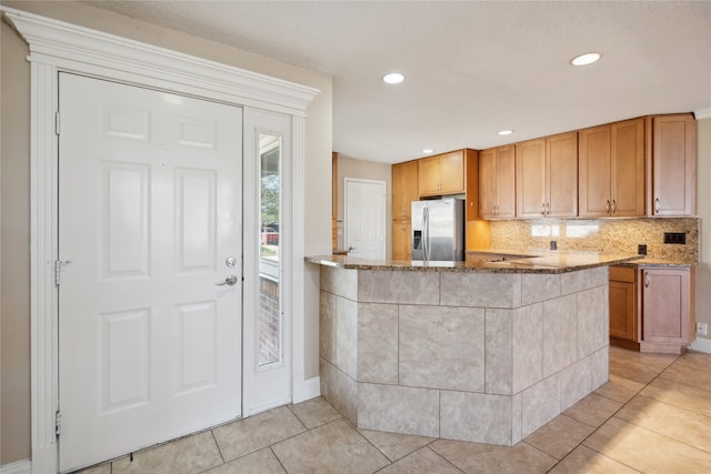 kitchen with light stone counters, kitchen peninsula, tasteful backsplash, light tile patterned floors, and stainless steel fridge with ice dispenser