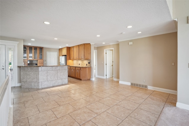 kitchen featuring tasteful backsplash, ornamental molding, a textured ceiling, stainless steel refrigerator, and light tile patterned floors