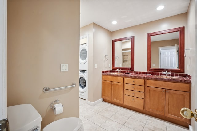 bathroom featuring stacked washer and dryer, tile patterned flooring, vanity, and toilet