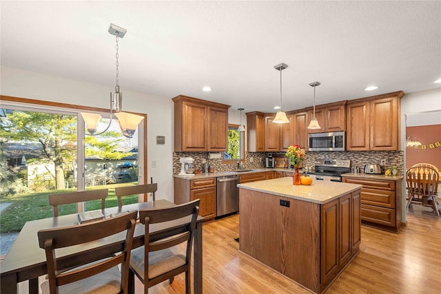 kitchen with pendant lighting, appliances with stainless steel finishes, a kitchen island, and light hardwood / wood-style flooring