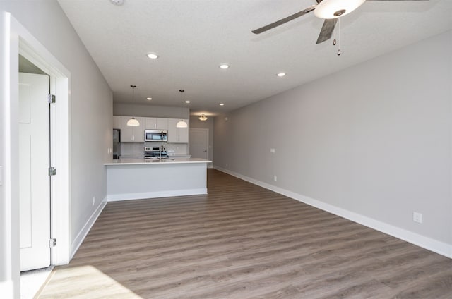 kitchen featuring white cabinetry, kitchen peninsula, appliances with stainless steel finishes, hanging light fixtures, and hardwood / wood-style floors