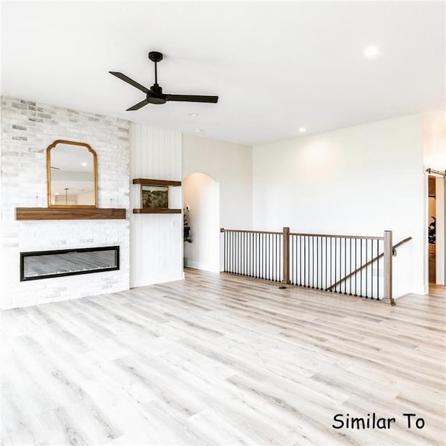 unfurnished living room with ceiling fan, a large fireplace, and light hardwood / wood-style floors