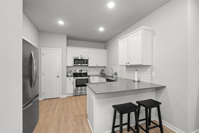 kitchen with kitchen peninsula, white cabinetry, sink, and appliances with stainless steel finishes