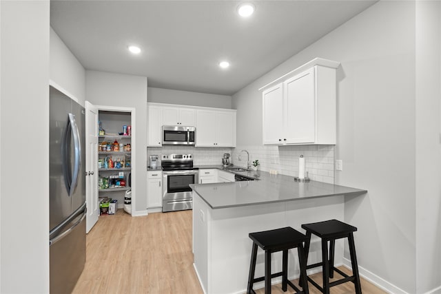 kitchen featuring sink, stainless steel appliances, kitchen peninsula, white cabinets, and light wood-type flooring