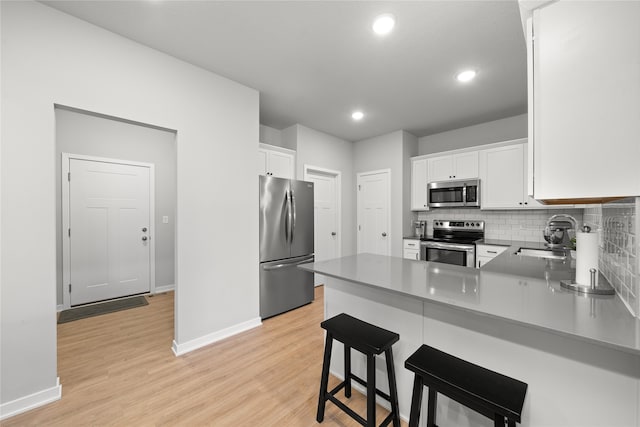 kitchen with kitchen peninsula, stainless steel appliances, sink, white cabinets, and light hardwood / wood-style floors