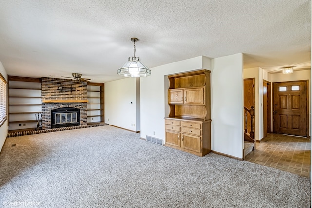 unfurnished living room with a fireplace, a textured ceiling, built in shelves, and dark carpet