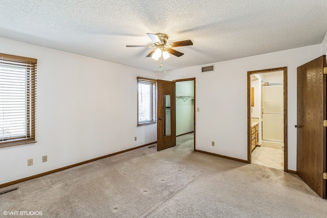 unfurnished bedroom with a spacious closet, ensuite bath, multiple windows, and ceiling fan