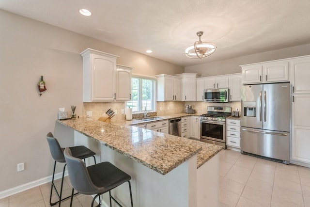 kitchen with stainless steel appliances, tasteful backsplash, white cabinets, a sink, and a peninsula