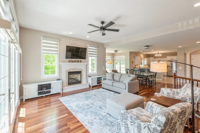 living room featuring recessed lighting, light wood-style floors, a glass covered fireplace, a ceiling fan, and baseboards