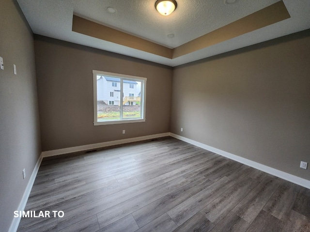 spare room with light wood-type flooring, a textured ceiling, and a raised ceiling