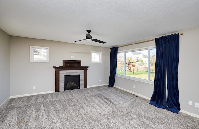 unfurnished living room featuring a tiled fireplace, ceiling fan, plenty of natural light, and carpet