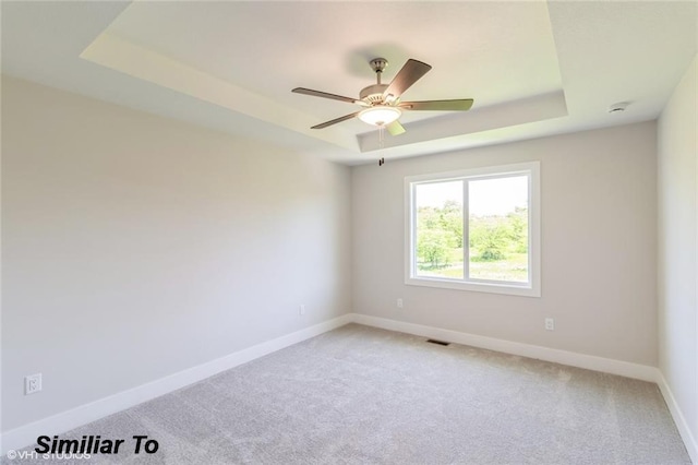 carpeted empty room with ceiling fan and a tray ceiling