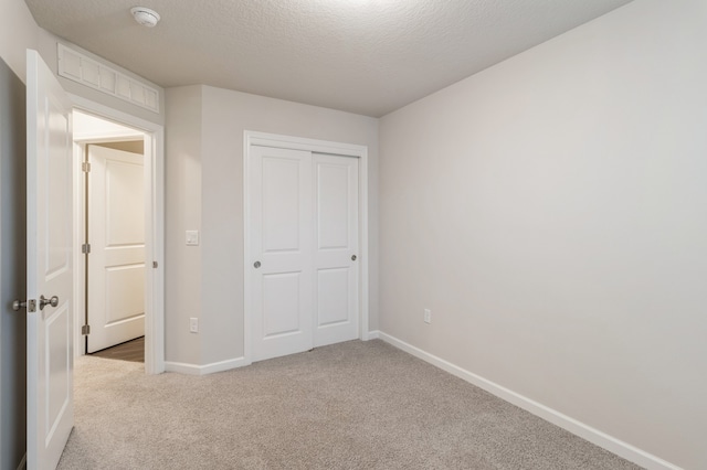 unfurnished bedroom with carpet floors, a closet, visible vents, a textured ceiling, and baseboards